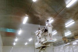 Coating inspector at work on a West African industrial site — over-the-shoulder framing, no visible face, clipboard and thickness gauge in hand
